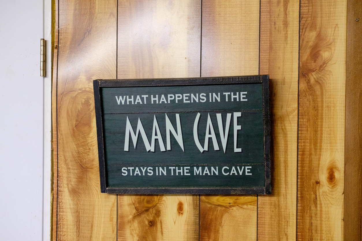 A sign hanging on a wooden door that says: What happens in the man cave stays in the man cave.